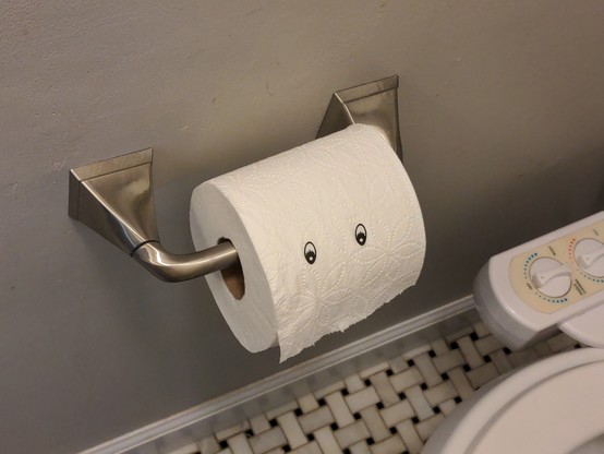 A roll of toilet paper in a metal wall holder. There are two eye stickers on the roll.