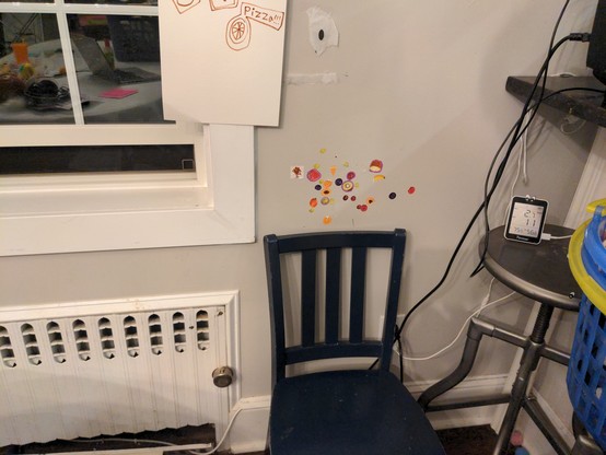 On the left (above a radiator), a single-hung window open about 5 inches. Along with various "artwork" on the walls (lol, kids), next to the window there's a blue chair and then a metal stool and the AQI monitor on the stool; probably about 4 feet away from the window? The AQI monitor's display reads PM2.5 @ 2.7 , while AQI is 11. The AQI monitor also has a pair of eye stickers on it because, again, lol kids.