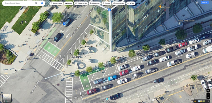 Google satellite imagery of the intersection of Boylston St & Brookline Ave. Still way too many fucking cars, but now there's protected bike lanes (flex posts) with green kermit bike boxes at the intersection. The low-rise warehouse is gone, replaced by a big glass tower office building or something.