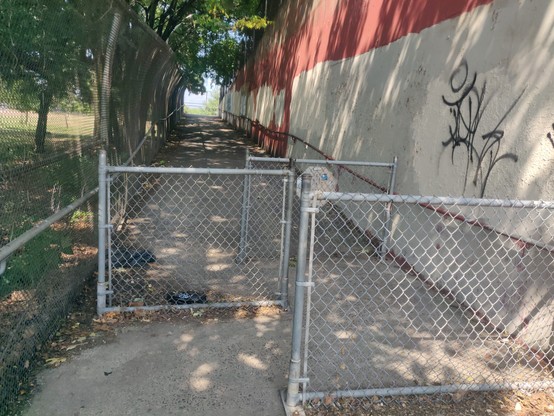A pedstrian overpass entrance, showing 3 offset chain-link fences close together so that you can barely fit a bike (or stroller/wheelchair, for that matter).